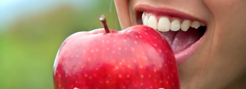 smiling woman biting into a red apple