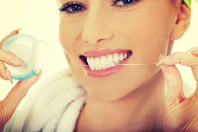 smiling woman using dental floss on her front teeth